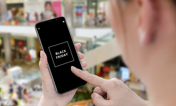 Black friday with smartphone. Woman holding cellphone with black friday text, Shopping mall in background.