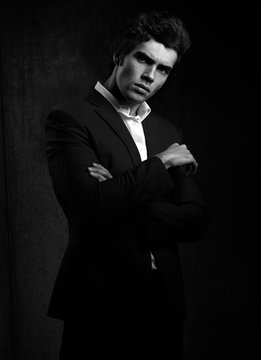 Handsome male model posing in fashion suit and white style shirt looking on dark shadow background. Black and white portrait