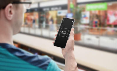 Man use mobile phone with Black friday test. Shopping mall in background.