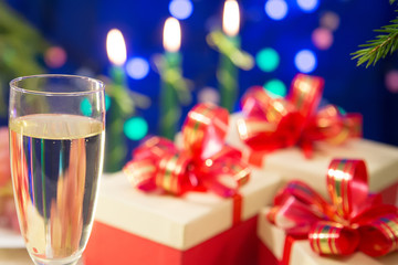 on the table a glass filled with champagne on a dark blue background with blurred lights. near there are New Year's gifts decorated with red bows. horizontal
