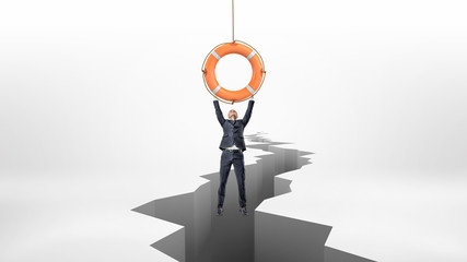 A tiny businessman holds on to a red life buoy hanging above a large earthquake rift.