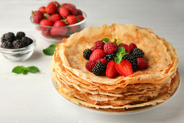 Plate of delicious thin pancakes with berries on wooden table