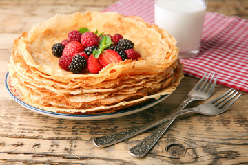 Plate of delicious thin pancakes with berries on wooden table