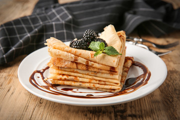 Plate with delicious thin pancakes and berries on wooden table