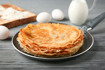 Pan with delicious thin pancakes on wooden table