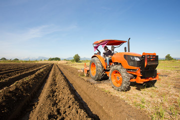 Obraz premium Close-up of agriculture red tractor cultivating field over blue sky