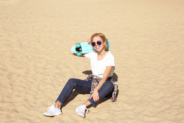 Attractive hipster girl with skateboard on sand