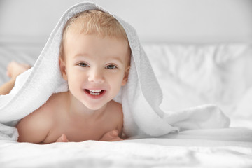 Cute little boy with towel on bed at home