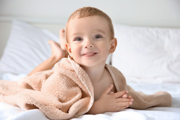 Cute little boy with towel on bed at home