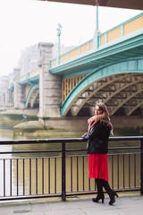 The young elegant pretty woman standing outdoor by the river and relying on railings