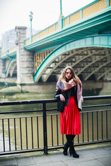 The young elegant attractive woman standing outdoor by the river and relying on railings