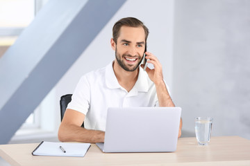 Attractive man with laptop talking on phone at home