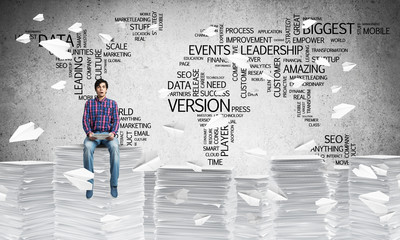 Attractive man sitting on pile of paper documents.