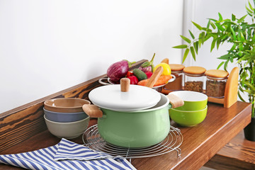 Stewpan, bowls and vegetables on wooden table in kitchen