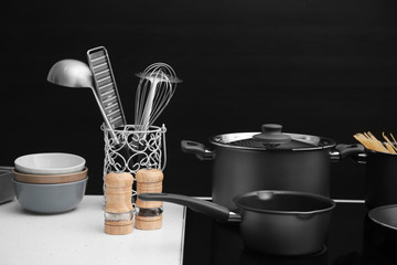 Different cooking utensils on electric stove against black background