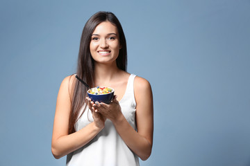 Young woman eating oatmeal on light background