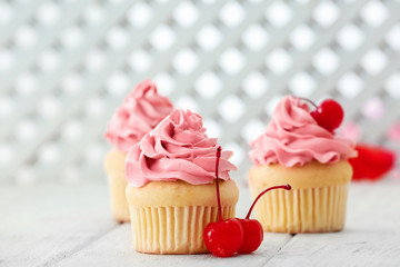 Delicious vanilla cupcakes and cherries on table