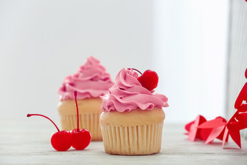 Delicious vanilla cupcakes and cherries on table