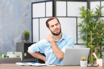 Tired young man using laptop in office