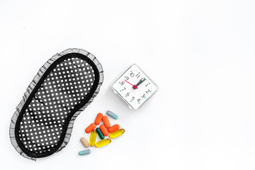 Sleeping pills for insomnia near sleep mask and alarm clock on white background top view copyspace