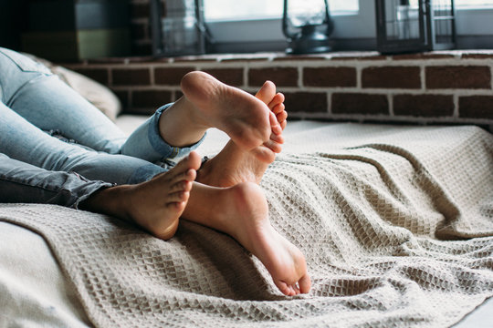 Young beautiful pair of lovers hug and kiss on the bed. Cropped image of lovers legs. People in jeans