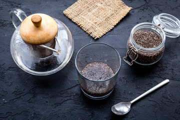 Brew chia seeds. Jar with seeds, scoop, bowl, tea pot with hot water. Black background