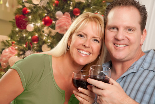 Caucasian Couple Holding Wine Glasses In Front of Decorated Christmas Tree.