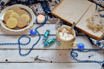 Christmas and new year holiday celebration concept background. Cup of cocoa with marshmallow, homemade chocolate cookie and peanut biscuit, lighted candles, xmas tree decoration on wooden table.