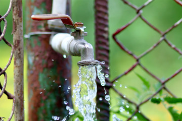 Close up of grunge brass faucet on green bokeh background. Water shortage and earth day concept.