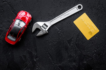 Pay for car repair. Wrench near car toys and bank card on black background top view copyspace