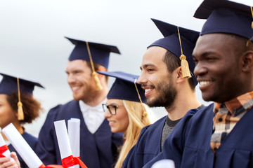 happy students in mortar boards with diplomas
