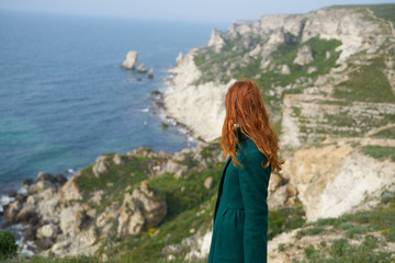 Naklejka premium Beautiful young woman standing on a cliff above the sea, mountains, nature