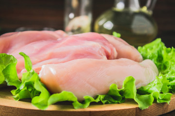 Raw chicken fillet and green salad on a round cutting board on a wooden table background. Meat ingredients for cooking.