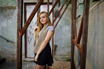 Young blonde girl in black skirt with scarf posed at street of city near the iron armor.