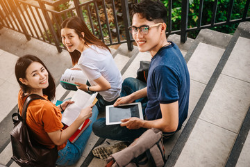 A group of young or teen asian student in university smiling and reading the book and look at the tablet or labtop computer in summer holiday.