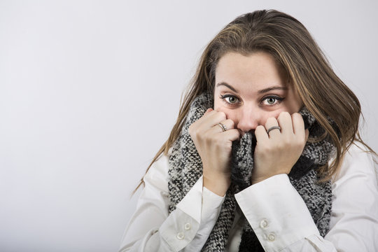 Ritratto di bella ragazza bionda e chiara che ci guarda tenendosi infreddolita la sciarpa con le mani sulla bocca - sfondo bianco
