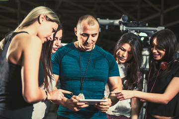 Smiling personal trainer using digital tablet while talking to group of women
