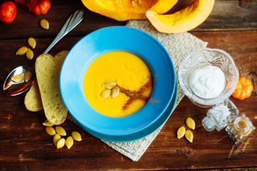 Pumpkin and carrot soup with cream and parsley on dark wooden background Top view