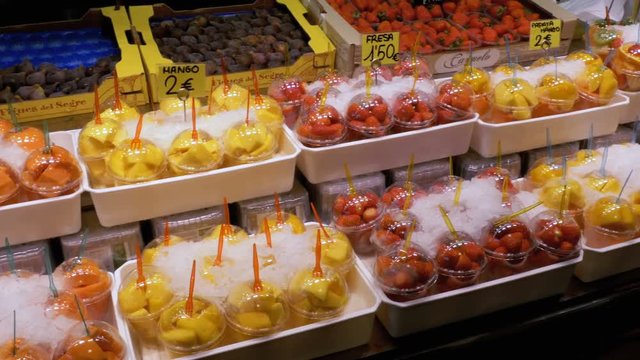 Showcase with Fruits in Ice at a Market in La Boqueria. Barcelona. Spain. Fruits in plastic cups on display at the market on the counter. Sliced Strawberry, kiwi, mango and other exotic fruits at