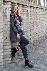 Portrait of a beautiful blonde woman in a gray coat near a brick fence that goes into the distance