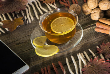 A cup of tea and a mobile phone on a vintage wood background.