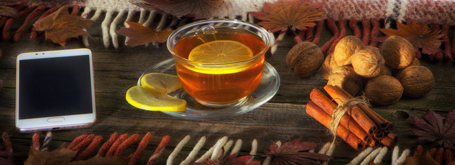 A cup of tea and a mobile phone on a vintage wood background.