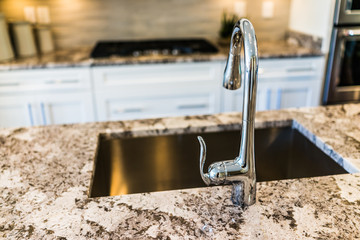 New modern faucet and kitchen sink closeup with island and granite countertops - obrazy, fototapety, plakaty