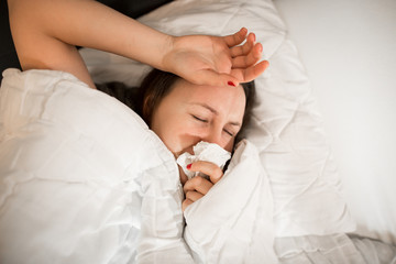 Pretty young brunette woman lying in the bed with handkerchief, looking sick and exhausted