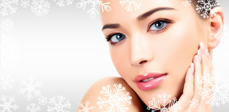 Closeup headshot portrait of a beautiful woman with beauty face and clean smooth soft skin , mild makeup. Grey steel background with snowflakes and a place for your information