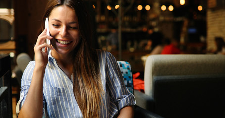 Beautiful lady sitting in a bar and smiling while holding a phon
