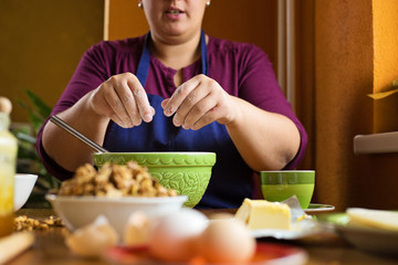 Close up photo of young beautiful adult woman with short hair, sitting behind a kitchen table, sifting the flour into the bowl, home baking concept
