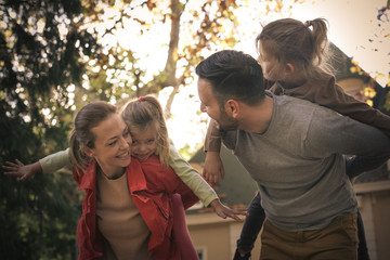 Happy parents carrying girls on piggyback. On the move.