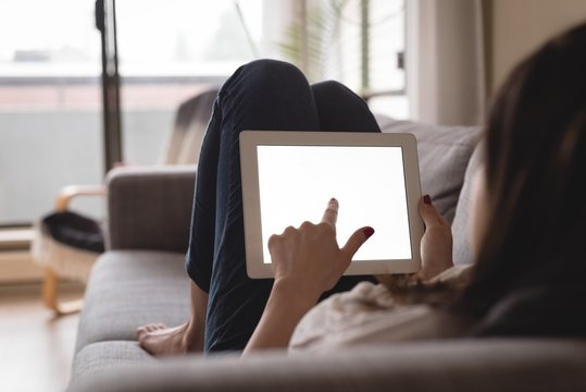Young woman using digital tablet while lying on sofa
