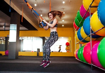 Fototapeta na wymiar Beautiful athletic woman doing exercises using trx in sportswear at gym